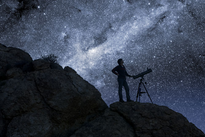 En person står på en klippe og ser opp på en stjerneklar nattehimmel gjennom et teleskop En person står på en klippe og ser opp på en stjerneklar nattehimmel gjennom et teleskop