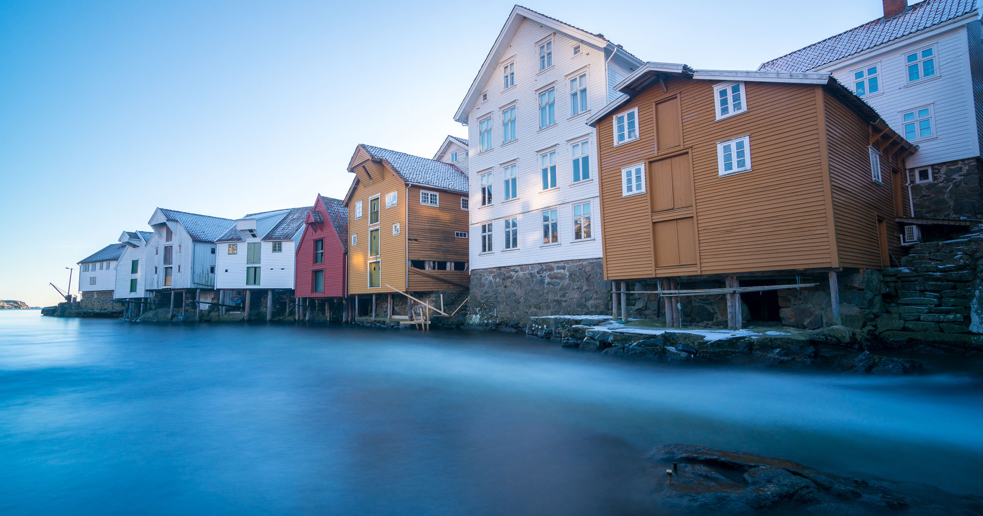 Fargerike trehus på påler ved en stille, blå sjø under en klar blå himmel