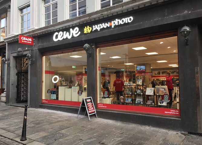 CEWE Japan Photo butikkfasade med store vinduer, hengende lamper og entréplass i en bygate CEWE Japan Photo butikkfasade med store vinduer, hengende lamper og entréplass i en bygate
