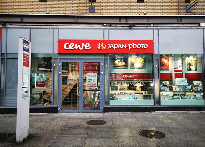 En butikkfasade med rød CEWE Japan Photo-logo, store glassvinduer og fremstilte fotoprodukter