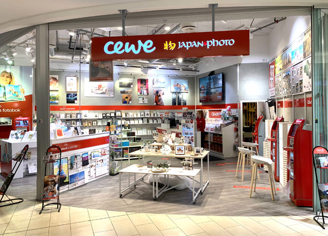 Butikkfront med CEWE Japan Photo-logo, lyse og moderne interiører, hyller med fotoprodukter og gaveartikler.