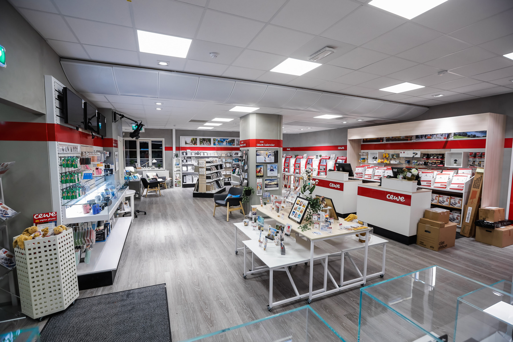 En lys og moderne CEWE-butikk med lyse tregulv, hyller fylt med fotoprodukter og gaveartikler, samt en innbydende diskområde En lys og moderne CEWE-butikk med lyse tregulv, hyller fylt med fotoprodukter og gaveartikler, samt en innbydende diskområde