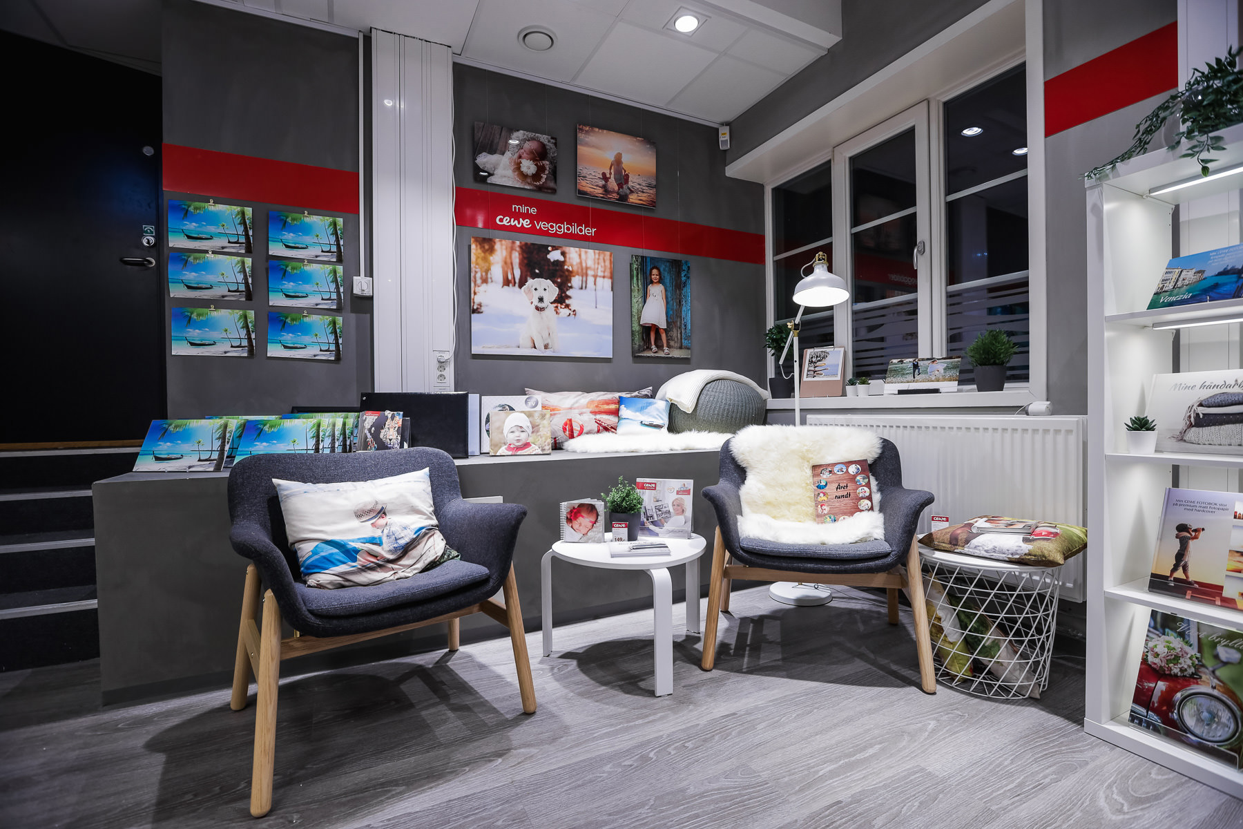 Et interiørbilde av en koselig butikkdel med to stoler, et rundt bord, og hyller fylt med fotobøker og dekor. Et interiørbilde av en koselig butikkdel med to stoler, et rundt bord, og hyller fylt med fotobøker og dekor.