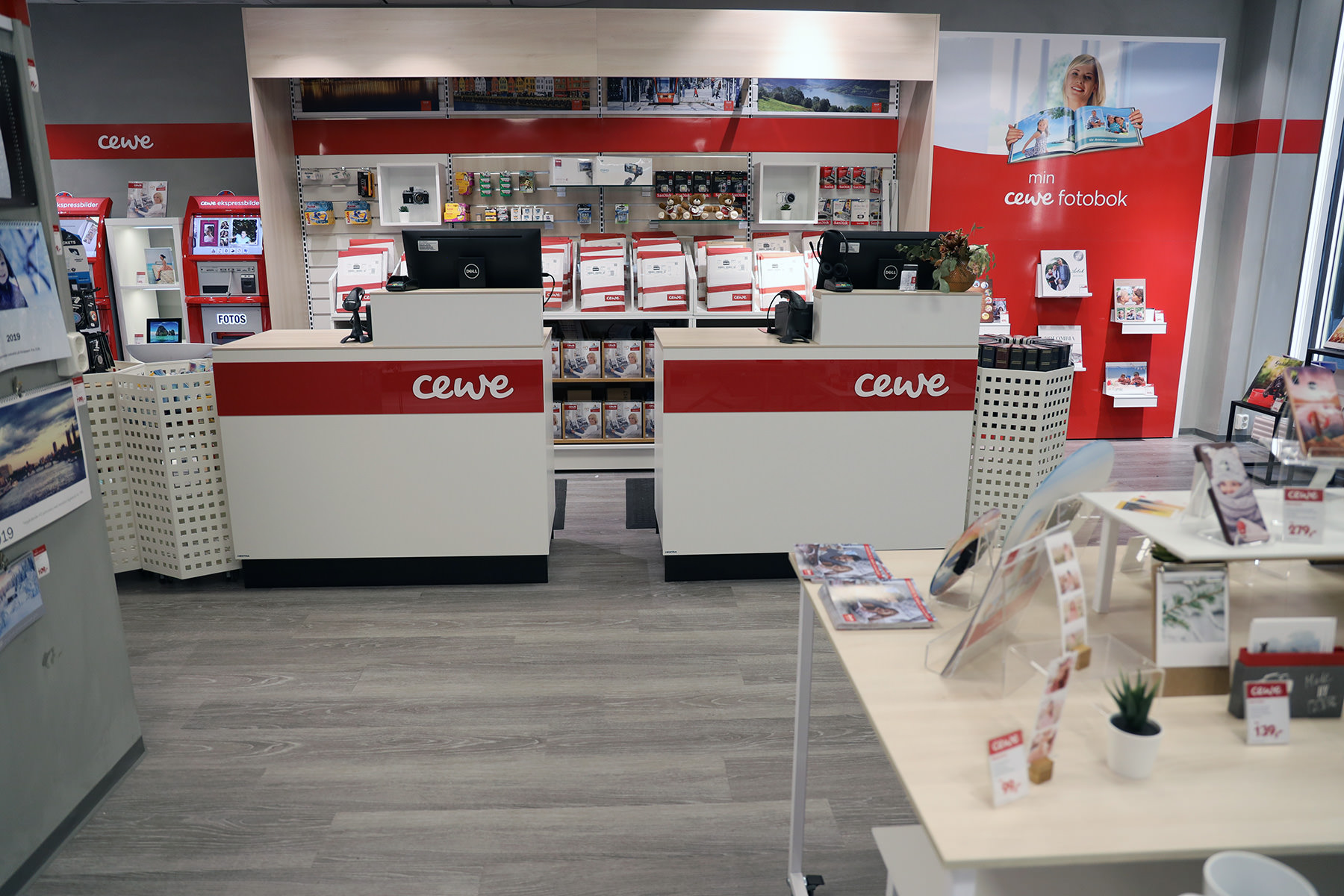 To skranker med CEWE-logo, omgitt av hyller fylt med fotoprodukter og trykkemateriell i en lys og moderne butikk. To skranker med CEWE-logo, omgitt av hyller fylt med fotoprodukter og trykkemateriell i en lys og moderne butikk.