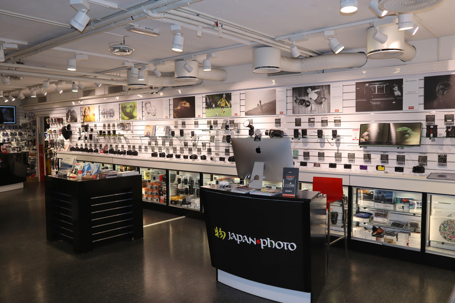 En lys og moderne fotobutikk med kameraer, linser og tilbehør organisert på vegger og i glassmontrer