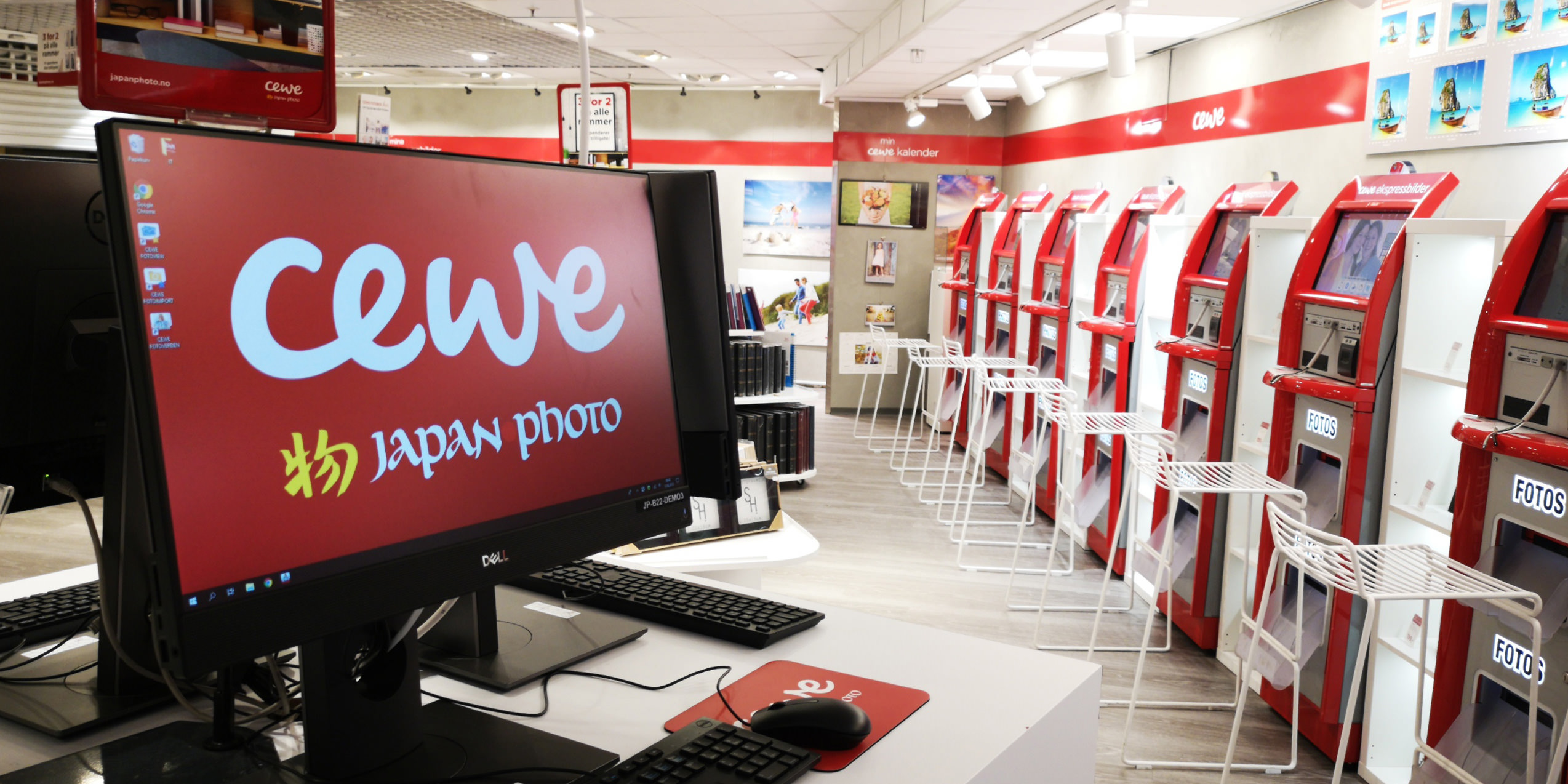 En lys og moderne butikk med CEWE fotokioskene i rødt til høyre og en dataskjerm med CEWE-logoen i forgrunnen