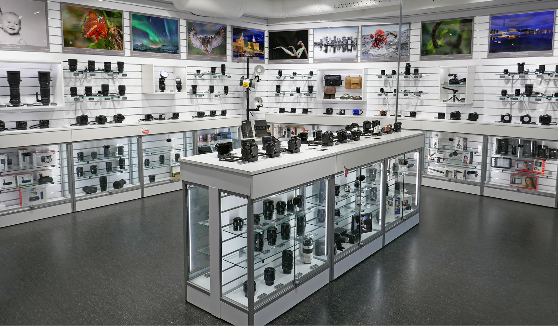 Butikkinnredning med hyller fylt av kameralinser, kameraer og fotoutstyr, oversiktlig presentert med opplyste glasskap og veggmonterte hyller