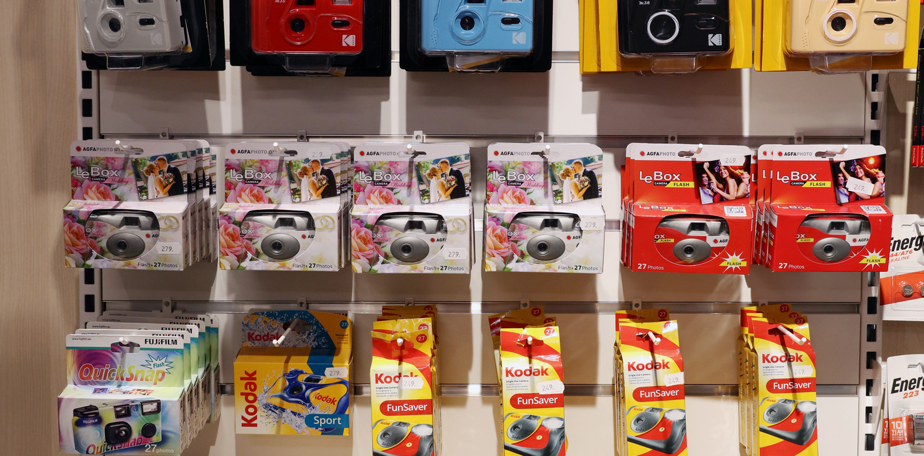 Engangskameraer fra AGFA, Kodak og Fujifilm i fargerike emballasjer, pent oppstilt i hyller. Engangskameraer fra AGFA, Kodak og Fujifilm i fargerike emballasjer, pent oppstilt i hyller.