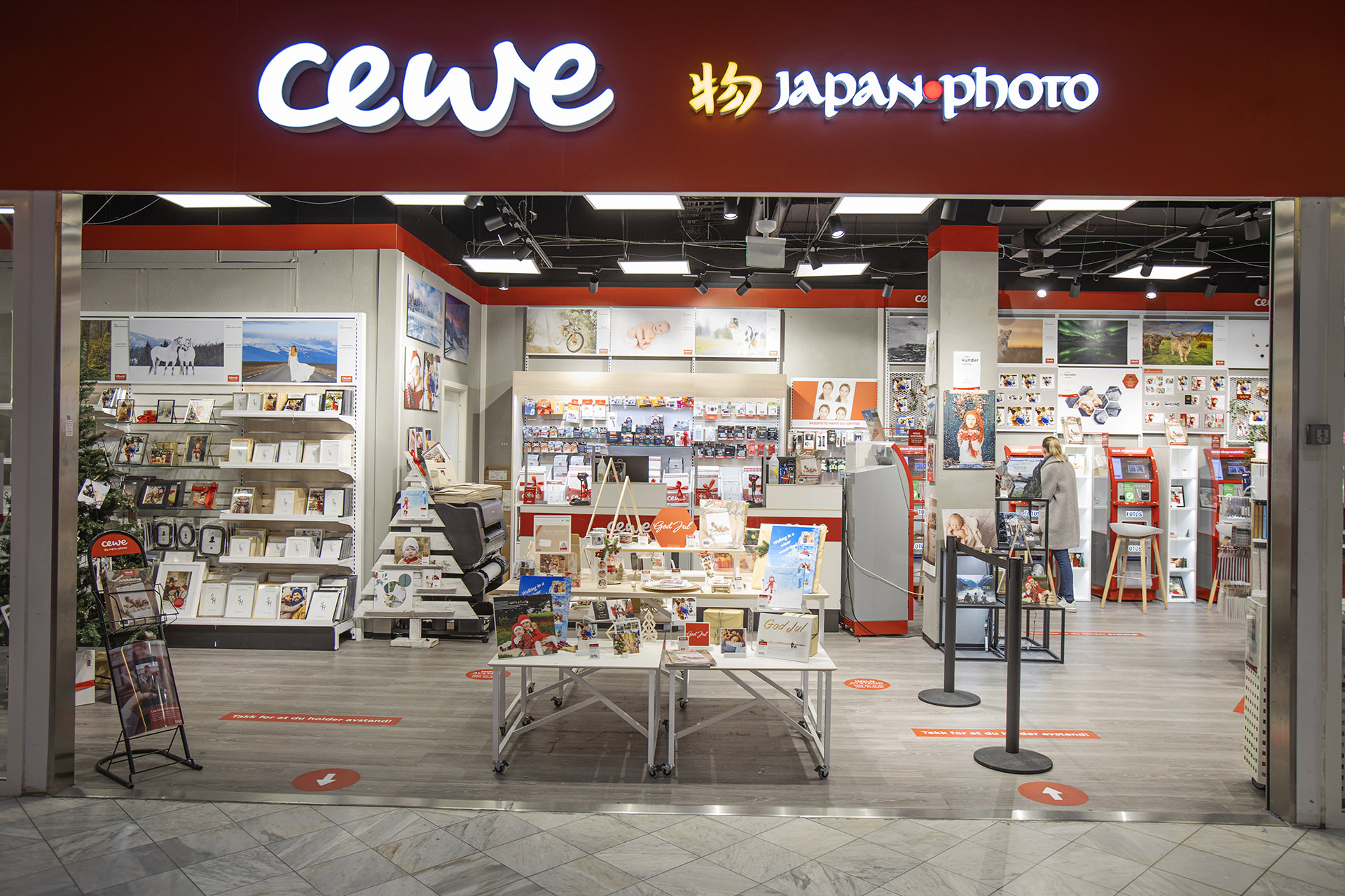 Butikkfasade av CEWE Japan Photo med opplyst logo, gaveprodukter og vegger fylt med fotoutstillinger og rammer Butikkfasade av CEWE Japan Photo med opplyst logo, gaveprodukter og vegger fylt med fotoutstillinger og rammer