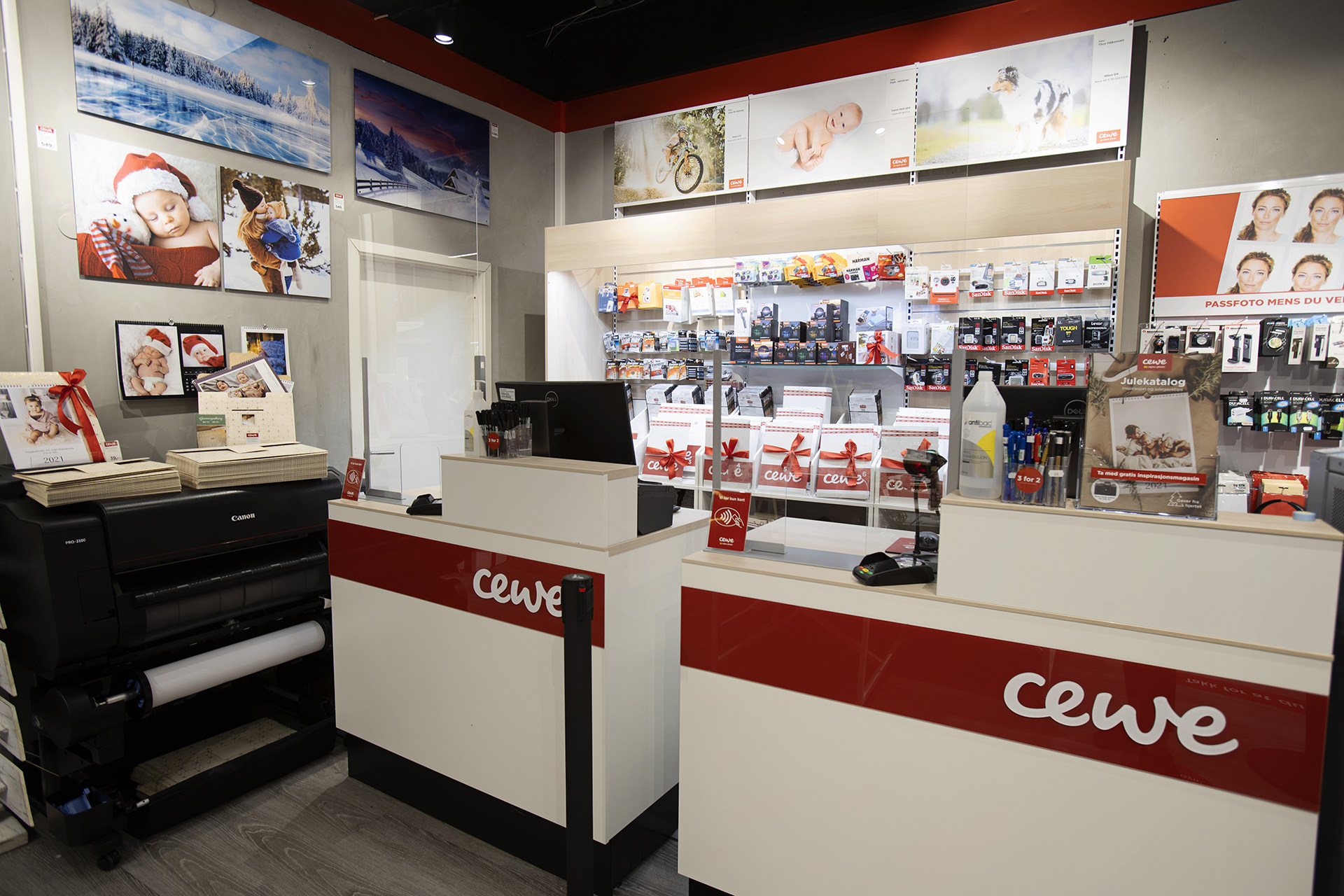 En lys og moderne CEWE-butikk med fotoskrivere, produkter i hyllene og innrammede bilder på veggen En lys og moderne CEWE-butikk med fotoskrivere, produkter i hyllene og innrammede bilder på veggen