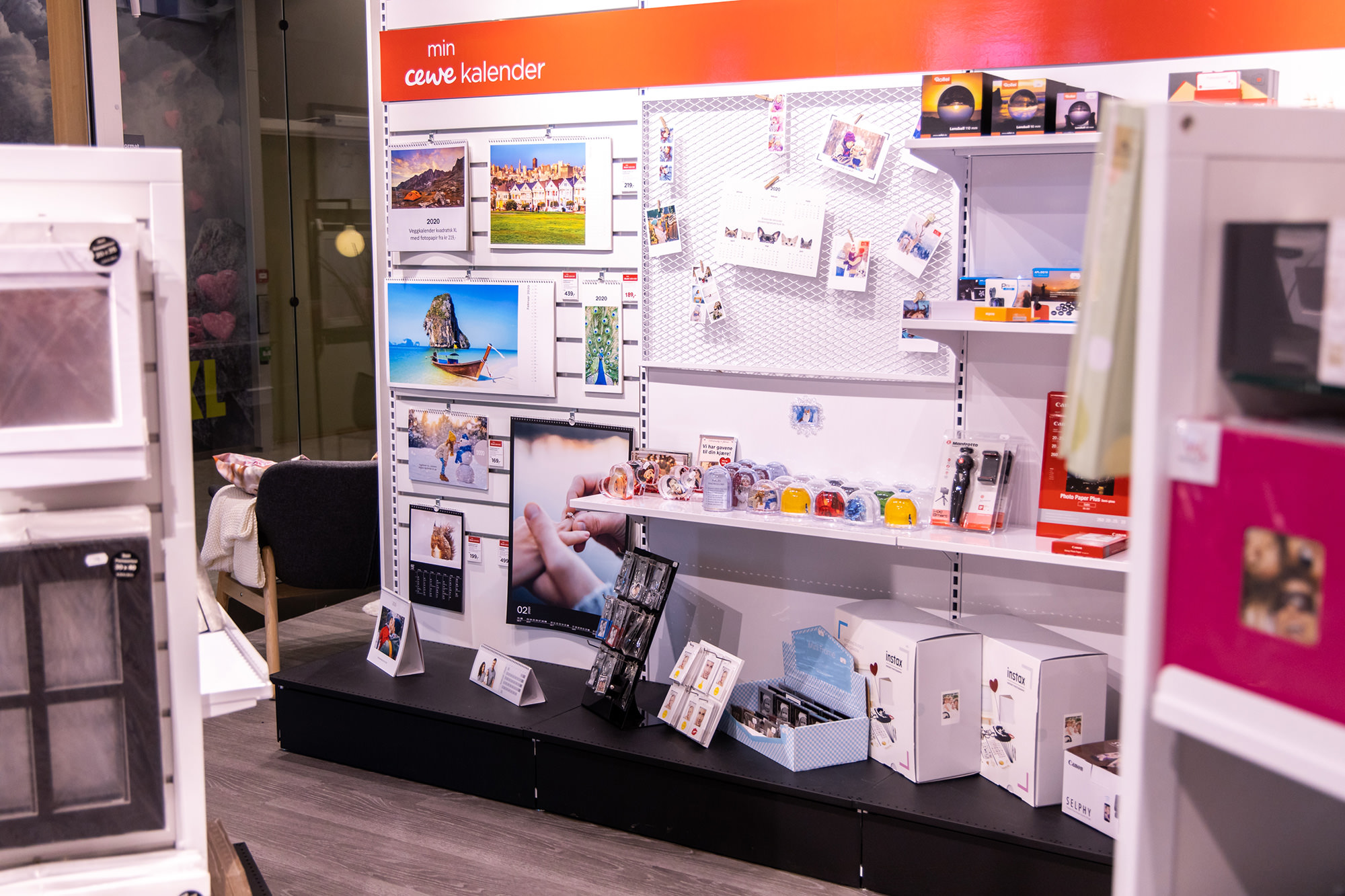 En butikkhylle med CEWE-produkter, inkludert fotokalendere, små gaveartikler og fotoutstyr. En butikkhylle med CEWE-produkter, inkludert fotokalendere, små gaveartikler og fotoutstyr.