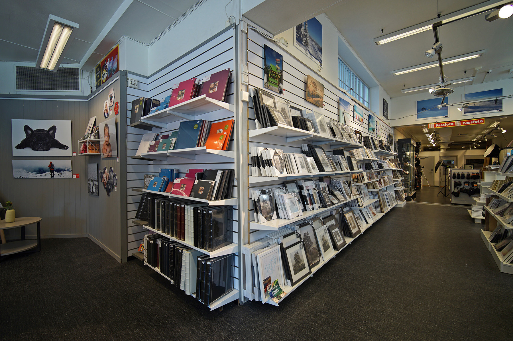 Reol med fargerike fotoalbum, rammer og lerretsbilder i en koselig butikkinnredning