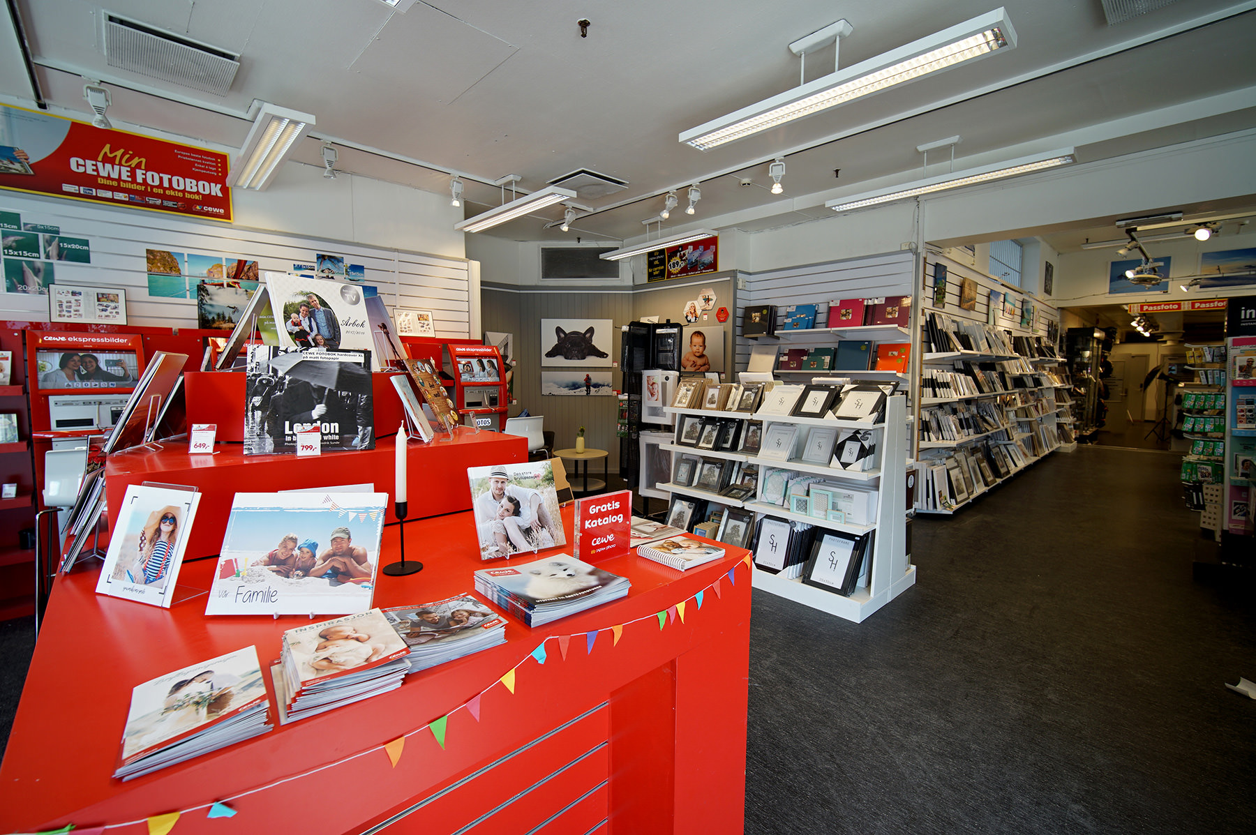 Lyse og vennlige butikklokaler med fotoprodukter, fotobøker og gaveartikler utstilt på røde og hvite hyller