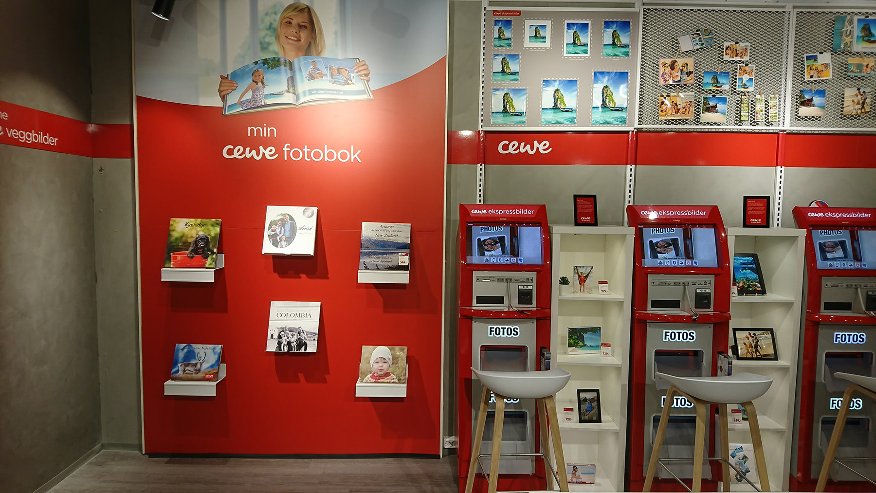 En utstillingsvegg med CEWE-produkter som fotobøker, veggbilder og fotoutskrifter, sammen med røde CEWE-selvbetjeningsautomater og hyller med dekorative bilder. En utstillingsvegg med CEWE-produkter som fotobøker, veggbilder og fotoutskrifter, sammen med røde CEWE-selvbetjeningsautomater og hyller med dekorative bilder.