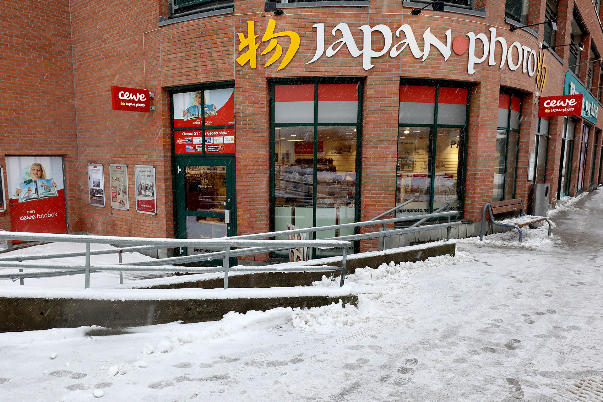 Butikklokale for Japan Photo med rød murvegg, store vinduer og inngang dekket av snø. Butikklokale for Japan Photo med rød murvegg, store vinduer og inngang dekket av snø.