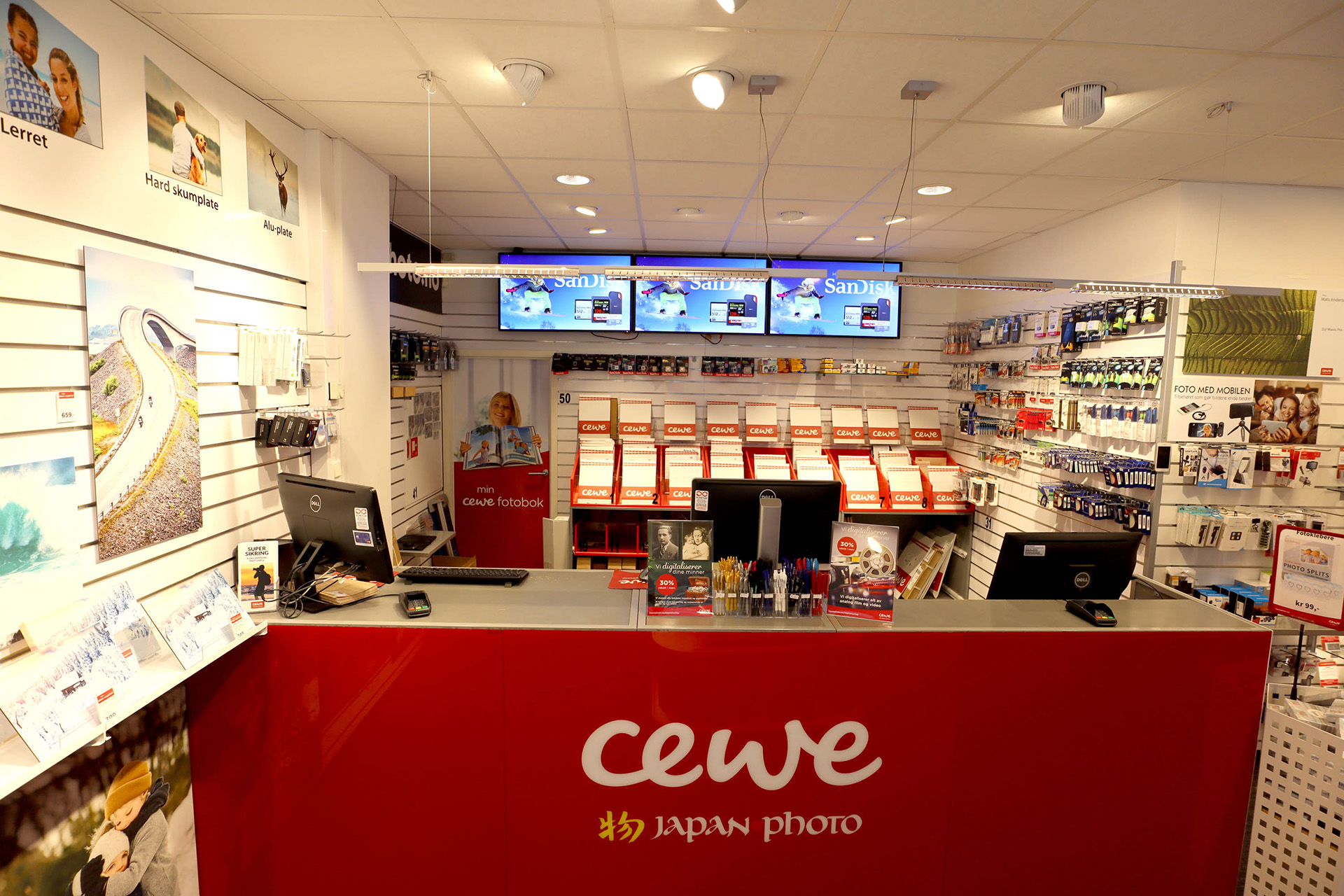 En lys og innbydende CEWE-butikk med røde detaljer, fotobokprodukter og teknisk tilbehør oppstilt på hyller. En lys og innbydende CEWE-butikk med røde detaljer, fotobokprodukter og teknisk tilbehør oppstilt på hyller.