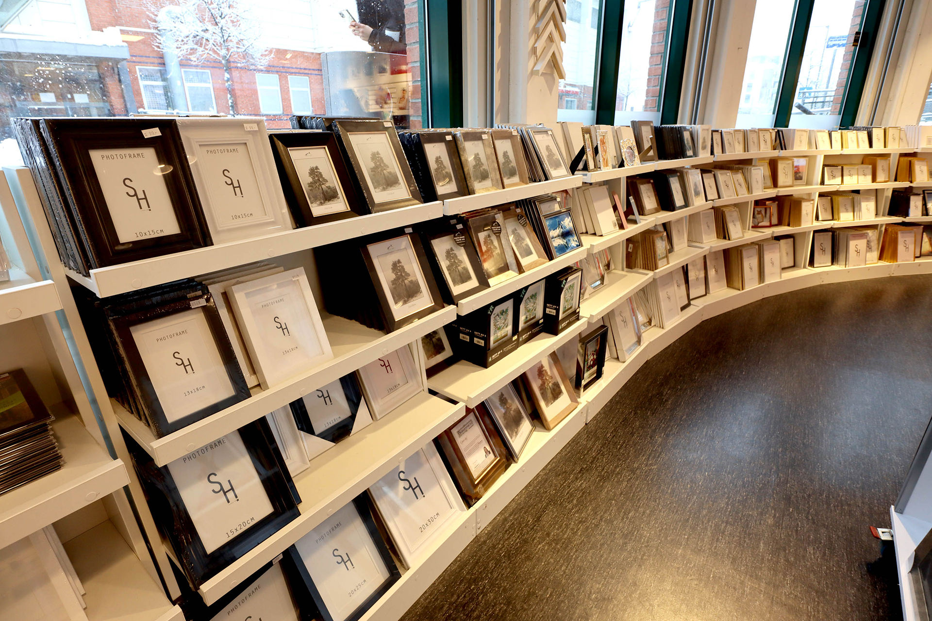 Hyller fylt med bilderammer i ulike størrelser og farger, plassert i et lyst butikklokale med store vinduer Hyller fylt med bilderammer i ulike størrelser og farger, plassert i et lyst butikklokale med store vinduer