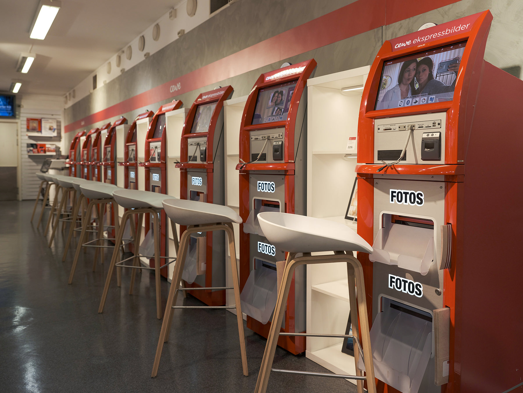 Serie med røde selvbetjente fotomaskiner i en lys butikk, ledsaget av høye, moderne stoler. Serie med røde selvbetjente fotomaskiner i en lys butikk, ledsaget av høye, moderne stoler.