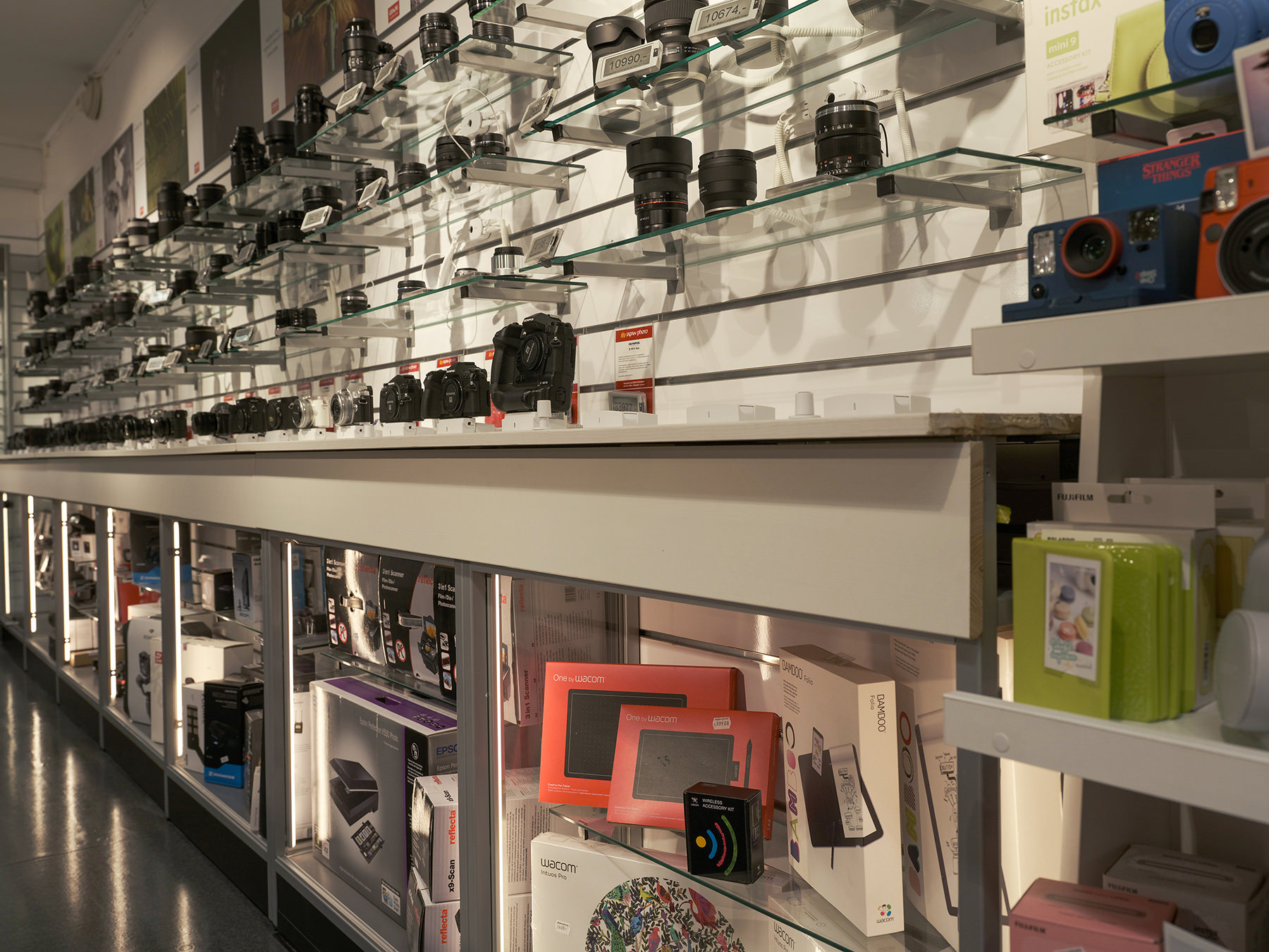 En rekke kameraer, linser og tilbehør som er pent utstilt på glasshyller i en godt opplyst butikk En rekke kameraer, linser og tilbehør som er pent utstilt på glasshyller i en godt opplyst butikk