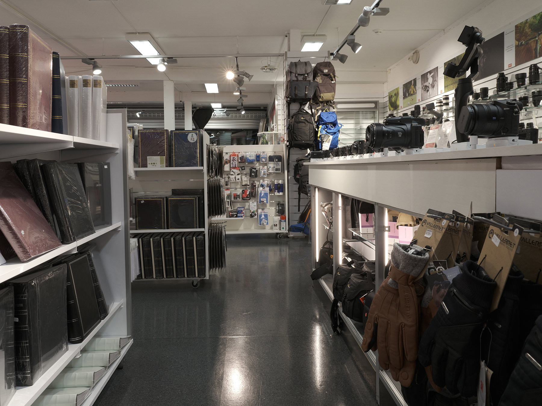 En butikk med fotoutstyr, inkludert kameraer, linser, fotovesker, fotoalbum og hansker, organisert på hyller og disker En butikk med fotoutstyr, inkludert kameraer, linser, fotovesker, fotoalbum og hansker, organisert på hyller og disker