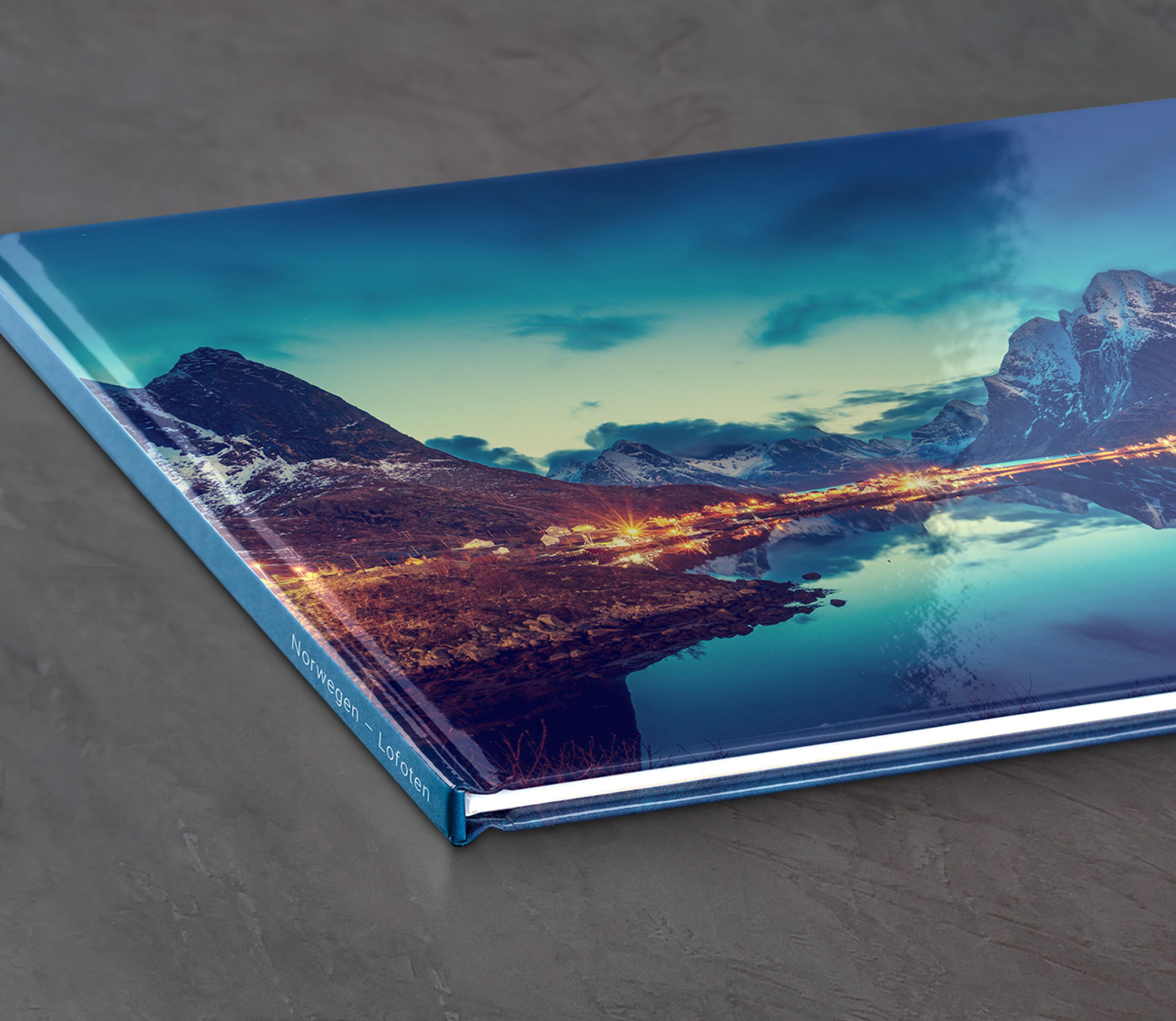 Fotobok med bilde av fjordlandskap i Lofoten, Norge, med lys fra hus som speiler seg i vannet under en klar, blå himmel