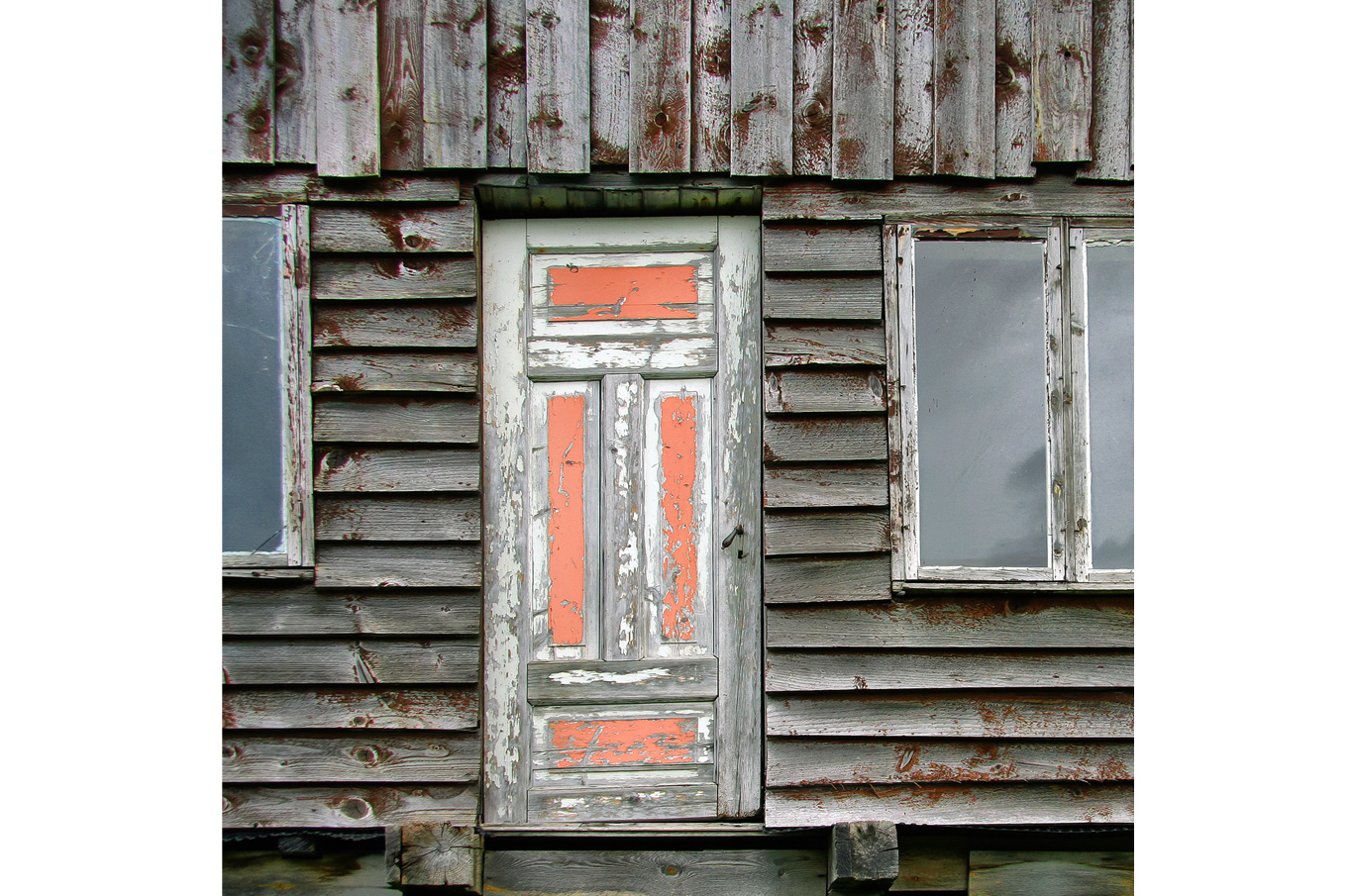 Slittende grå trevegg med en gammel, falmet treport og oransje malingsrester Slittende grå trevegg med en gammel, falmet treport og oransje malingsrester