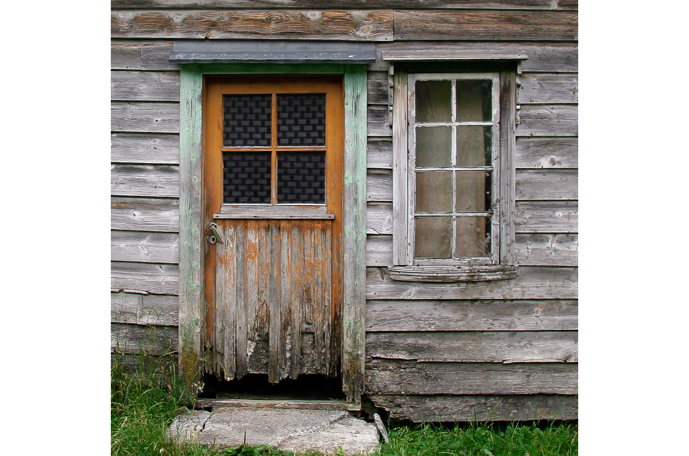 Slittet trehusfasade med en værbitt dør og et gammelt vindu med sprukne ruter Slittet trehusfasade med en værbitt dør og et gammelt vindu med sprukne ruter