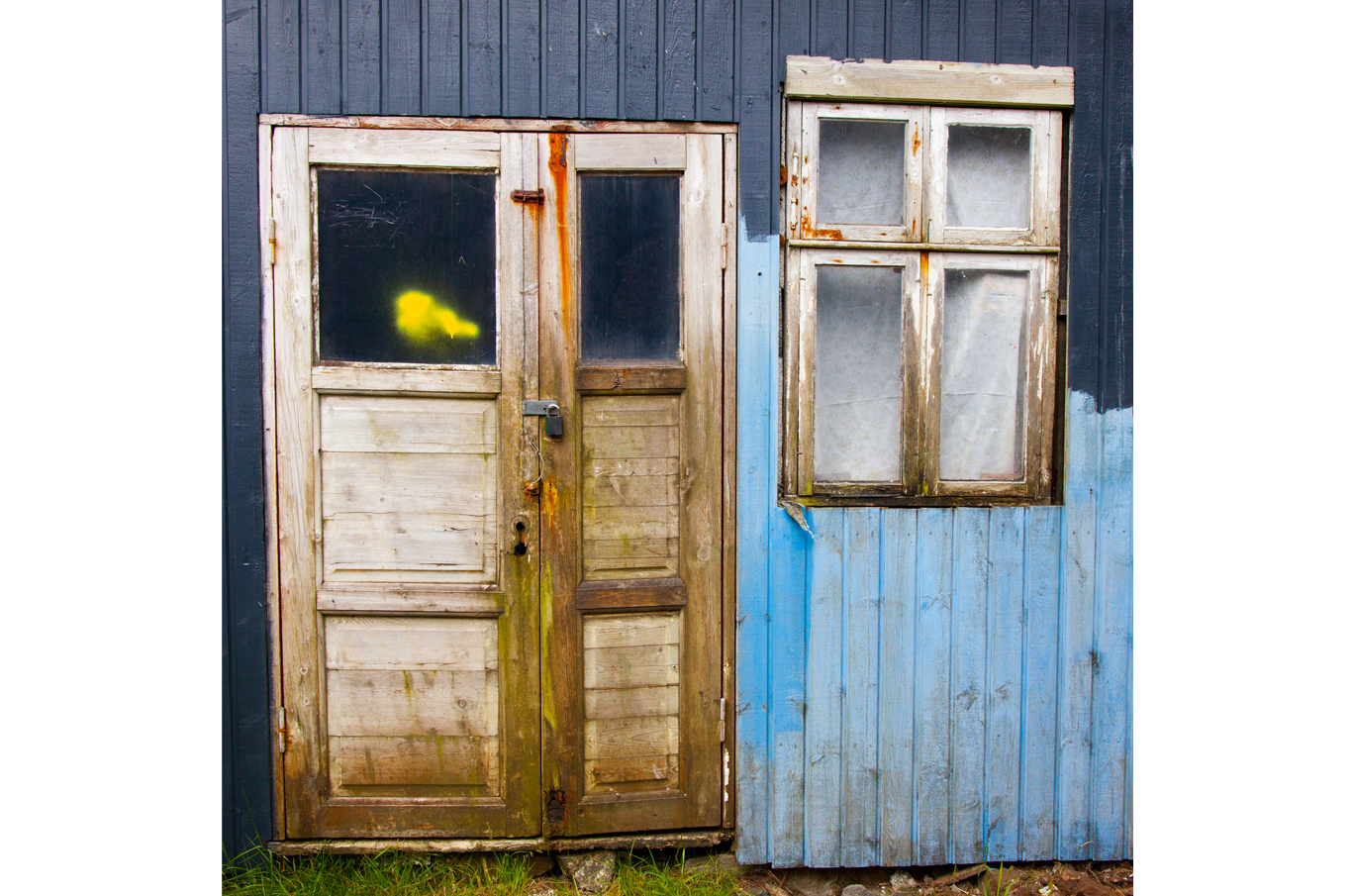 Slitt trebåtdør og vindu på en vegg med falmet blå maling og rustfarget detaljer Slitt trebåtdør og vindu på en vegg med falmet blå maling og rustfarget detaljer