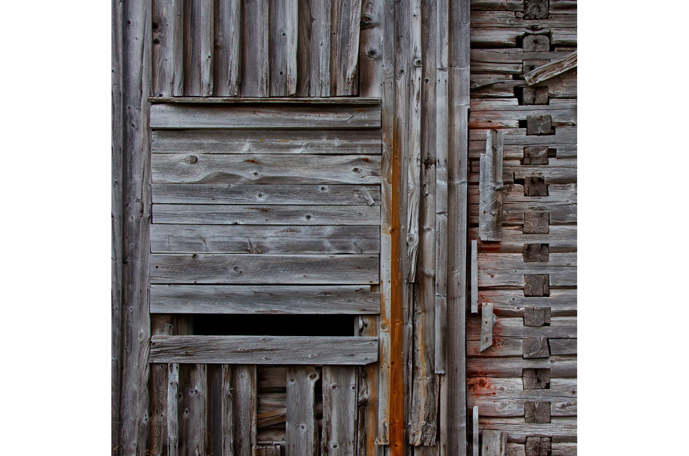 Gammel, grånet trevegg med detaljer av utskårne skjøter og en liten åpning i midten Gammel, grånet trevegg med detaljer av utskårne skjøter og en liten åpning i midten