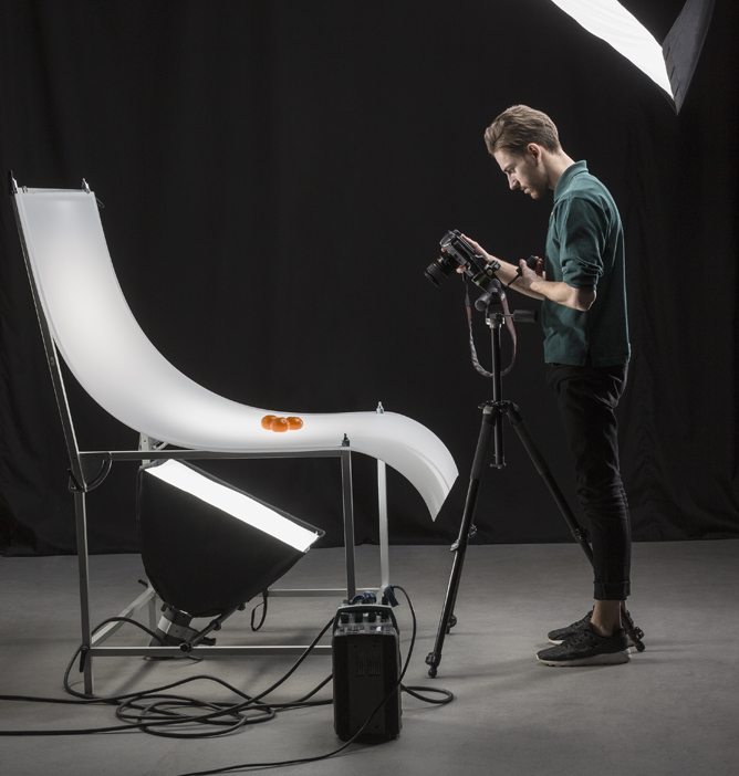 Fotograf tar bilde av mandariner på en hvit, bøyd overflate med profesjonelt studioutstyr