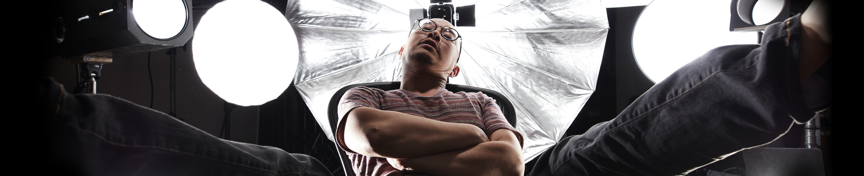 Person som sitter avslappet på en stol i et fotostudio, omgitt av lysutstyr og reflektorer.