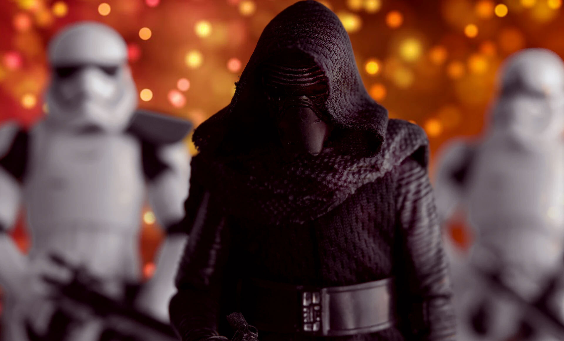 En skikkelse med sort kappe og hette, omgitt av to hvite stormtroopere, mot en bakgrunn med varme lys i gult og rødt