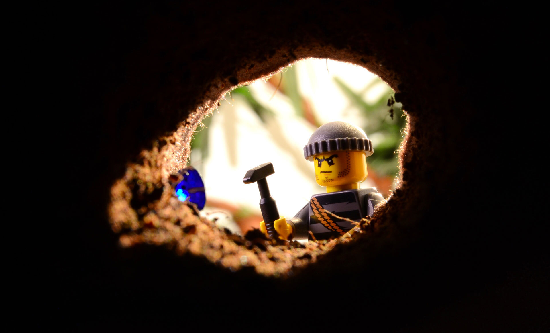 Lego-figur i gruvearbeiderantrekk holder en hammer, sett gjennom et rundt hull i jorden med lys bakgrunn