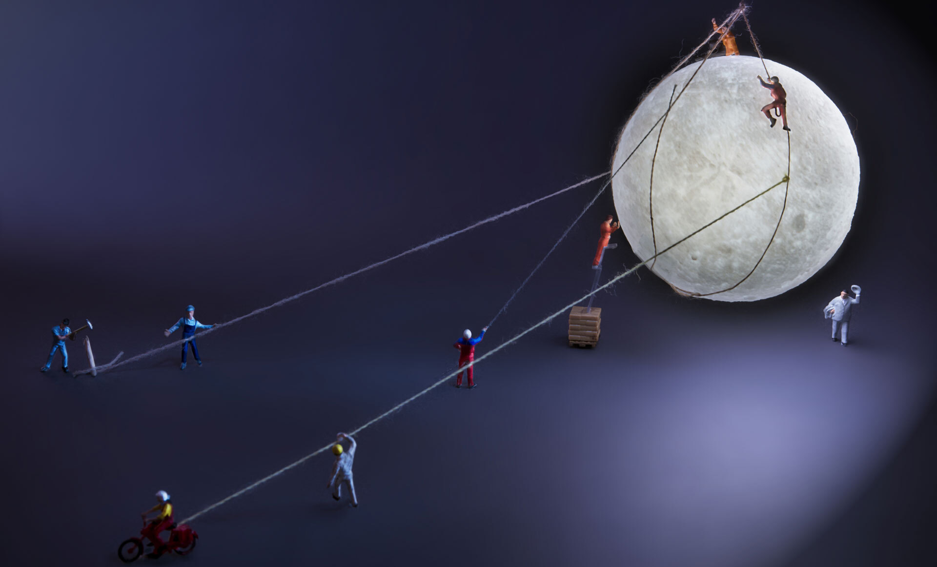 Små miniatyrfigurer samarbeider om å flytte en stor fullmåne ved hjelp av tau og stiger