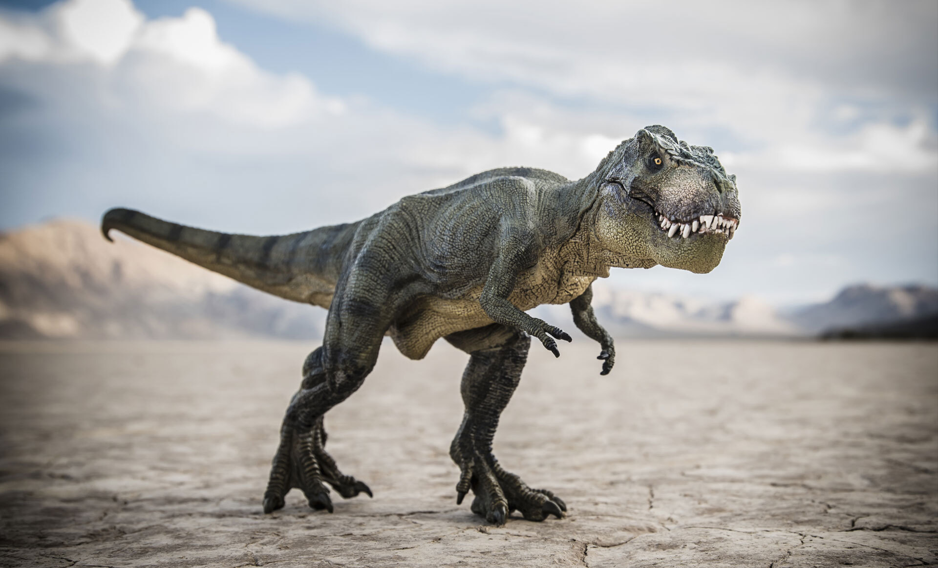 En modell av en T-rex står i et tørt ørkenlandskap med fjell i bakgrunnen