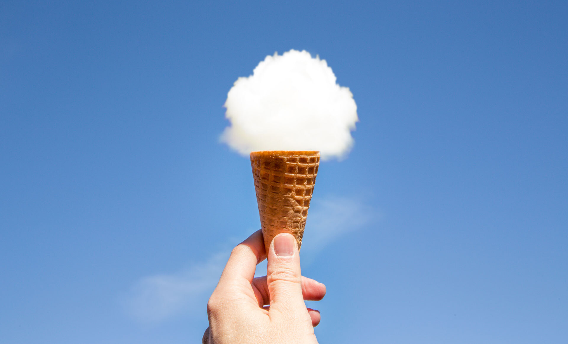 En hånd som holder en iskjeks under en sky som ligner på iskrem