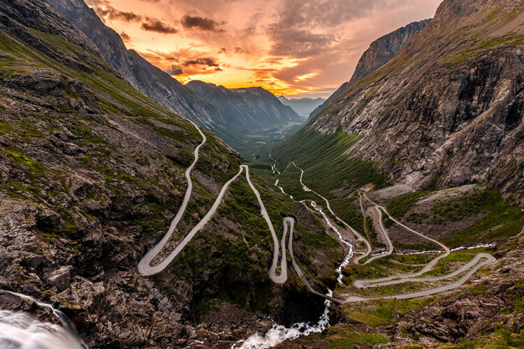 Svingete fjellvei i Trollstigen omringet av bratte fjellsider og en vakker solnedgang Svingete fjellvei i Trollstigen omringet av bratte fjellsider og en vakker solnedgang