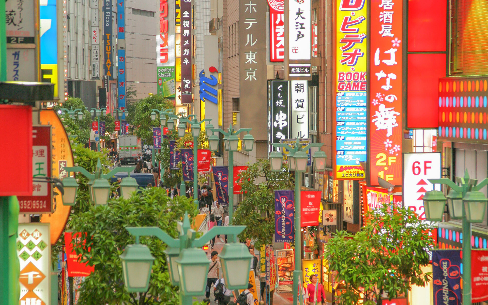 Fargerik gate i Tokyo med lysskilt, grønne gatelamper og folk som går mellom butikker