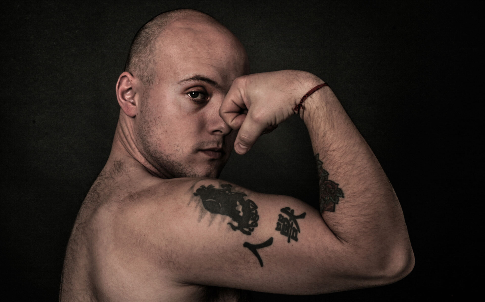 En person viser en muskuløs overarm med flere tatoveringer på en mørk bakgrunn