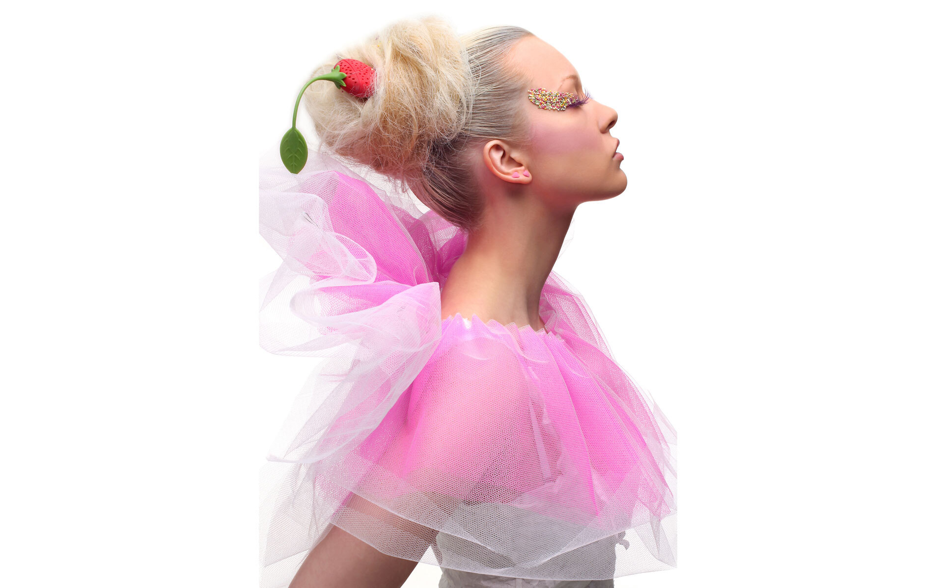 Kvinne med oppsatt hår dekorert med en jordbærformet hårpynt, iført tyll i lys rosa farge.