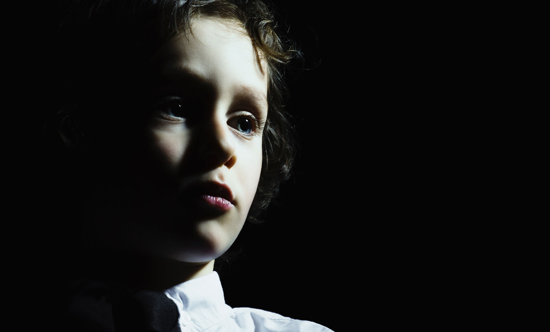 En person med krøllete hår på en svart bakgrunn, iført en hvit skjorte og sort slips