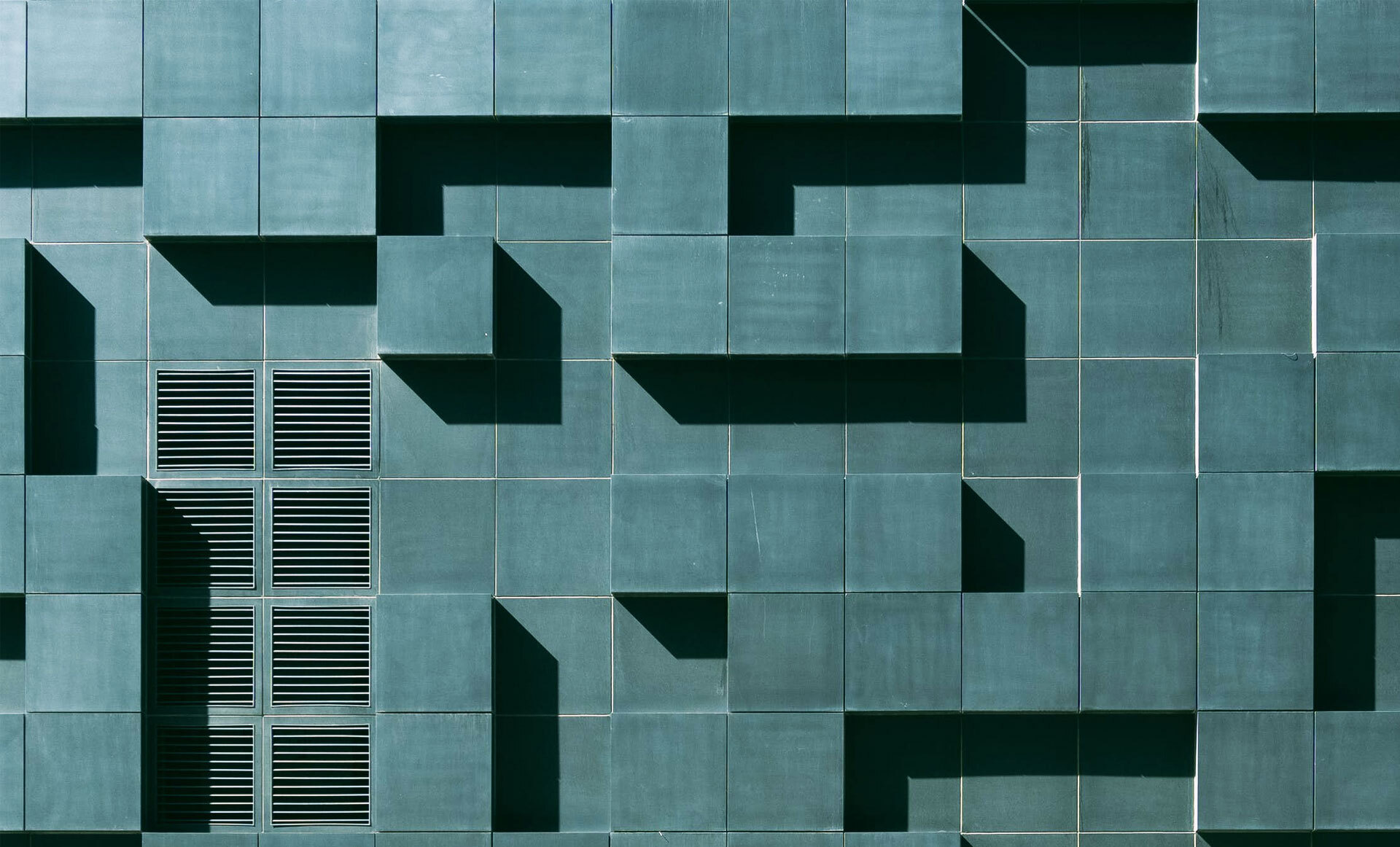 Grønn fasade med flislagt mønster av kvadrater og rektangler som skaper dybdeeffekt gjennom skygger