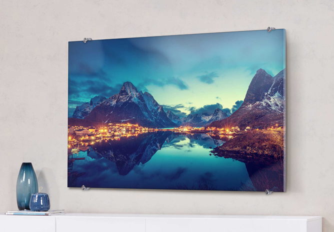 Et bilde av en fjord omringet av høye fjell, speilet i det rolige vannet, med lys fra en liten landsby ved vannkanten