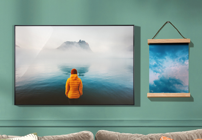 Person i oransje jakke står foran en rolig innsjø med tåke og et fjell i bakgrunnen