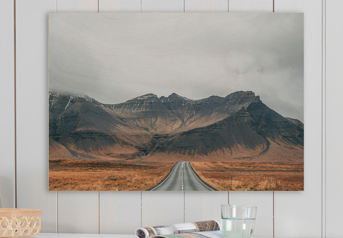 En lang, rett vei som leder mot fjell med dramatiske, mørke topper under en overskyet himmel