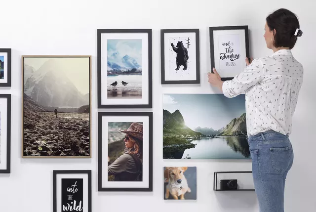 Kvinne ordner en bildekollasje på en vegg med naturfotografier, et hundebilde og inspirerende sitater