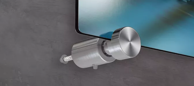 Metallisk veggfeste med rund skruknapp som holder et glassmotiv mot en grå vegg