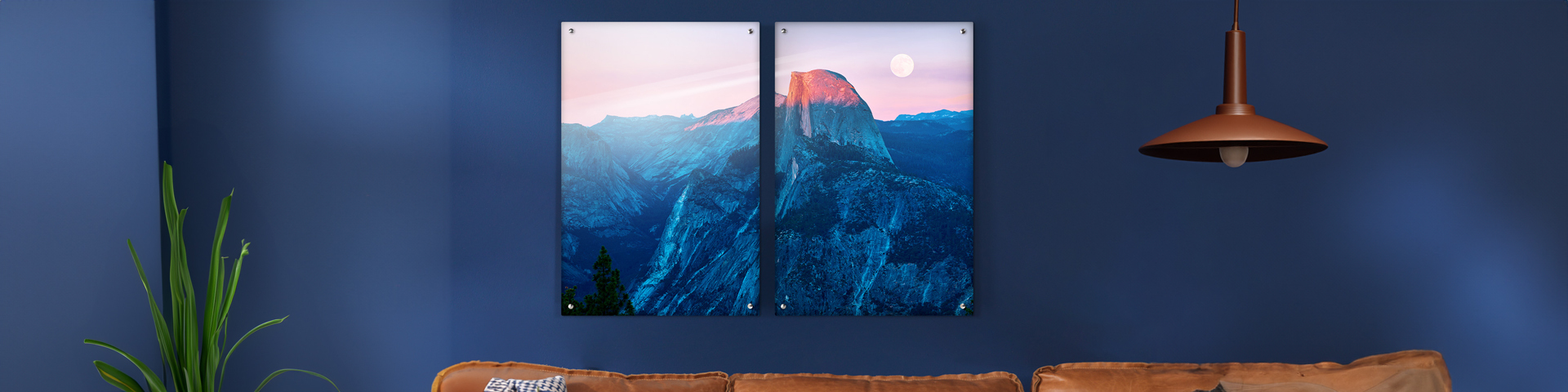 To fjellbilder i blå og rosa toner henger på en blå vegg over en brun skinnsofa