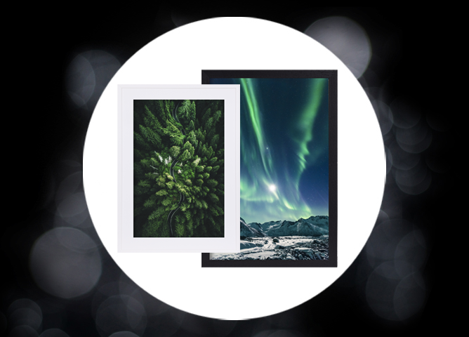 To innrammede bilder, det ene med en frodig grønn skog ovenfra i hvit ramme, det andre med nordlys over fjellandskap i svart ramme