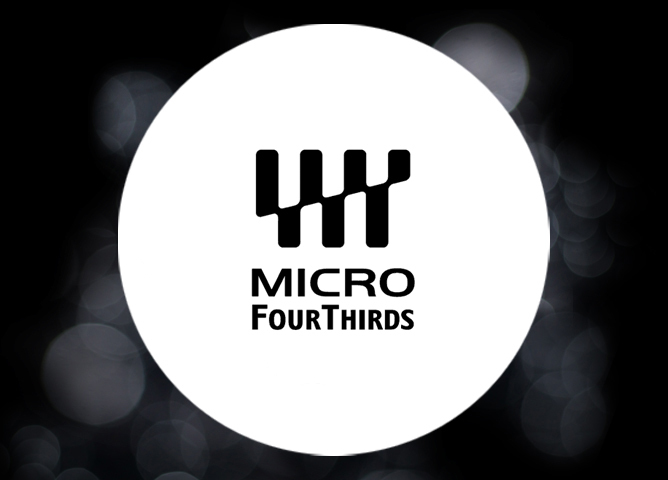 Logoet til Micro Four Thirds med svart tekst og stilisert symbol på hvit sirkel med uskarp svart bakgrunn